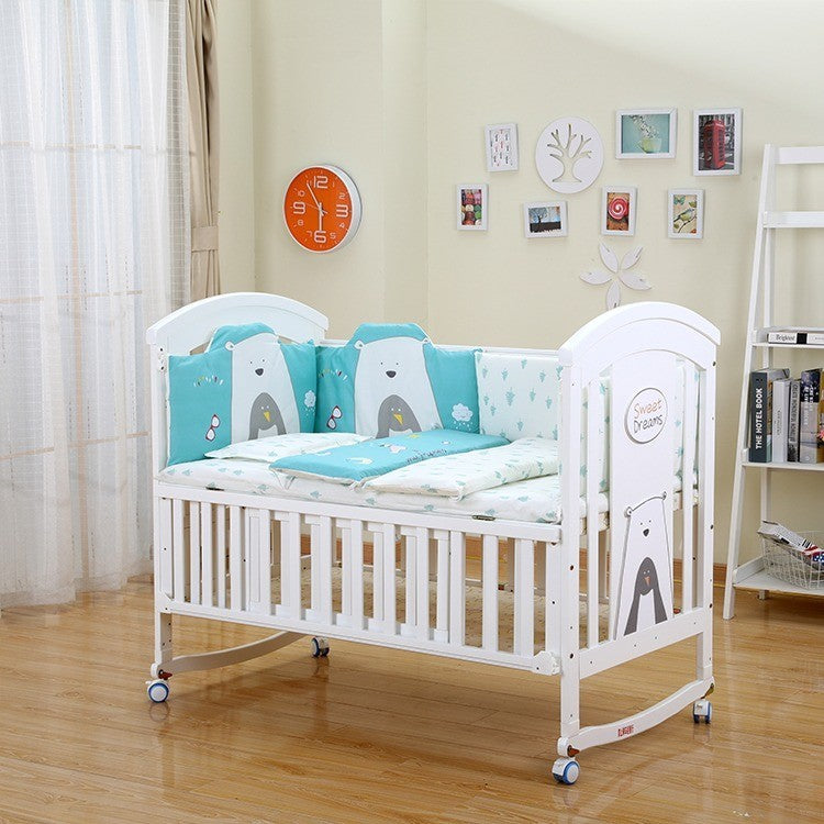 White crib with blue and gray bear-themed bedding in a room with a clock and bookshelf.