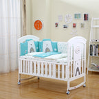 White crib with blue and gray bear-themed bedding in a room with a clock and bookshelf.