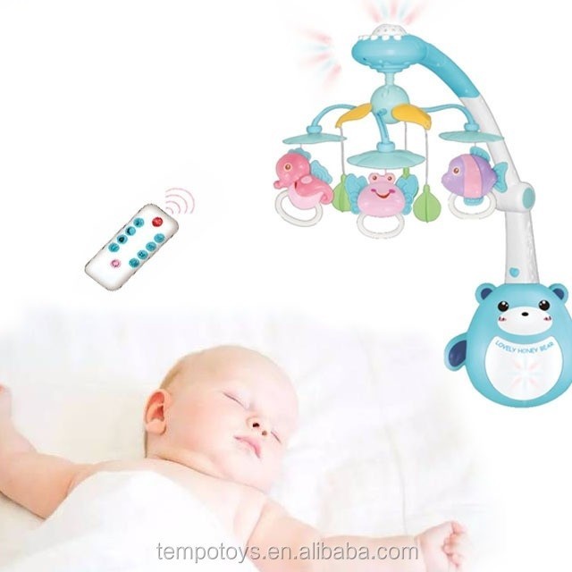 Baby sleeping next to a colorful baby crib mobile with remote control.