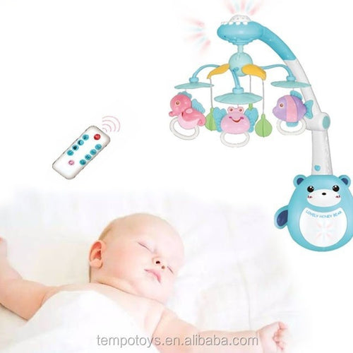 Baby sleeping next to a colorful baby crib mobile with remote control.