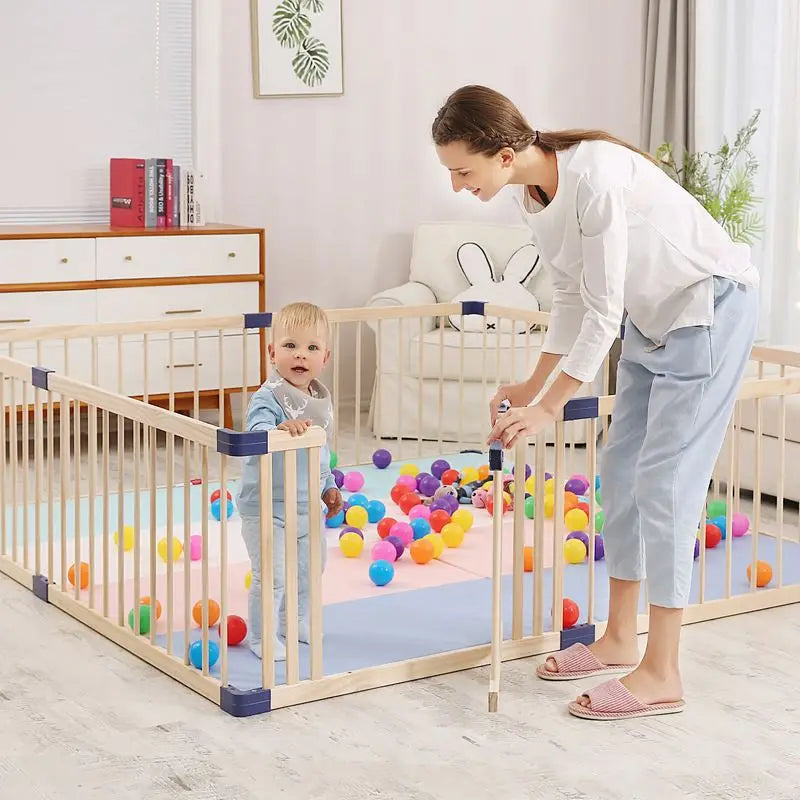 Woman and child playing with colorful balls inside a wooden playpen .