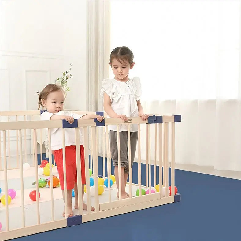 Two children standing behind a baby gate with colorful balls on the floor.