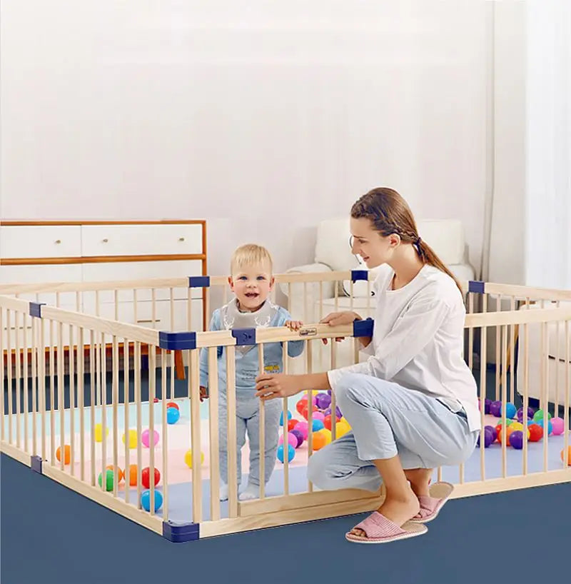 Woman and child playing with colorful balls inside a wooden playpen.