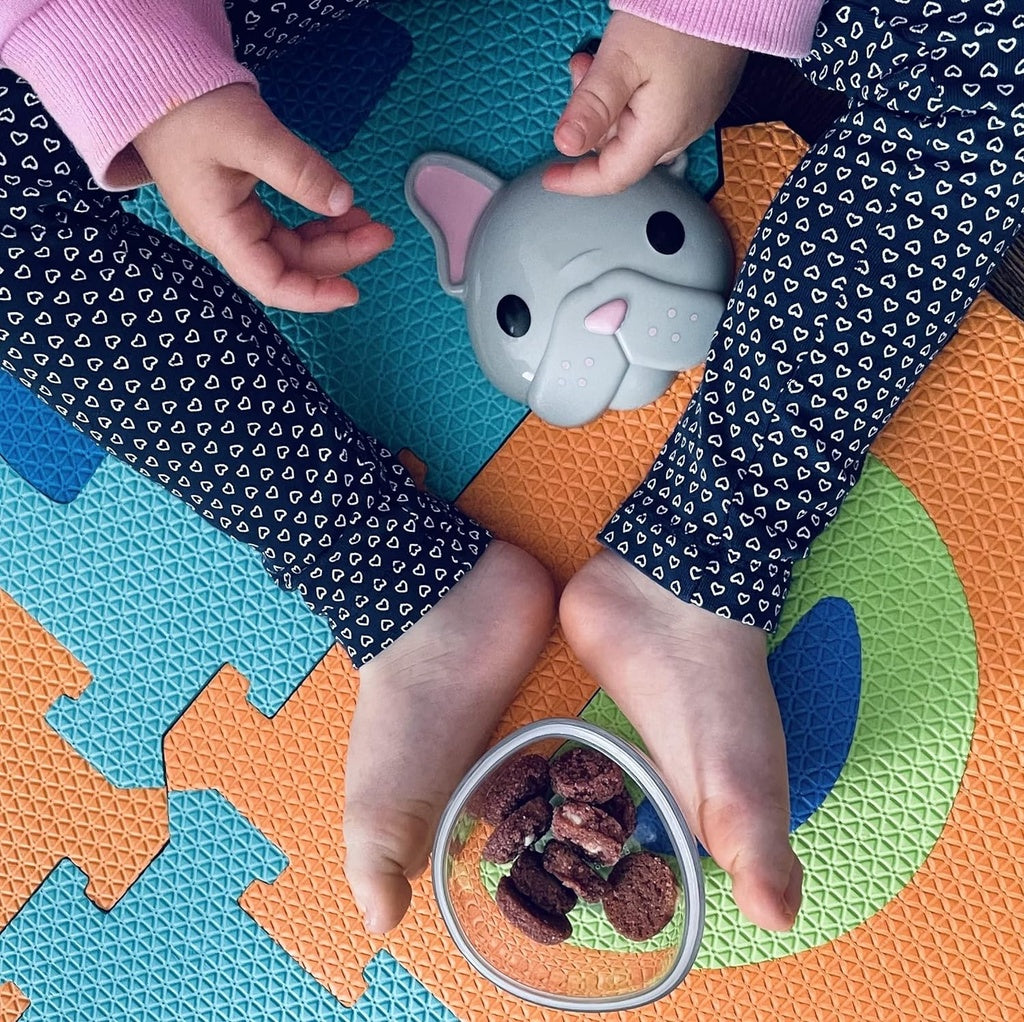 Child's hands holding a small Melli snack container of snacks on a colorful play mat.