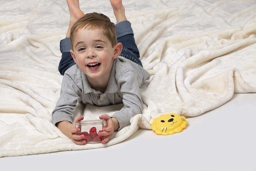 Child lying on a white blanket with a melii snack glass container of red berries and a smiley face toy.