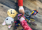 Children's hands playing with colorful pom-poms and art supplies on a wooden surface.