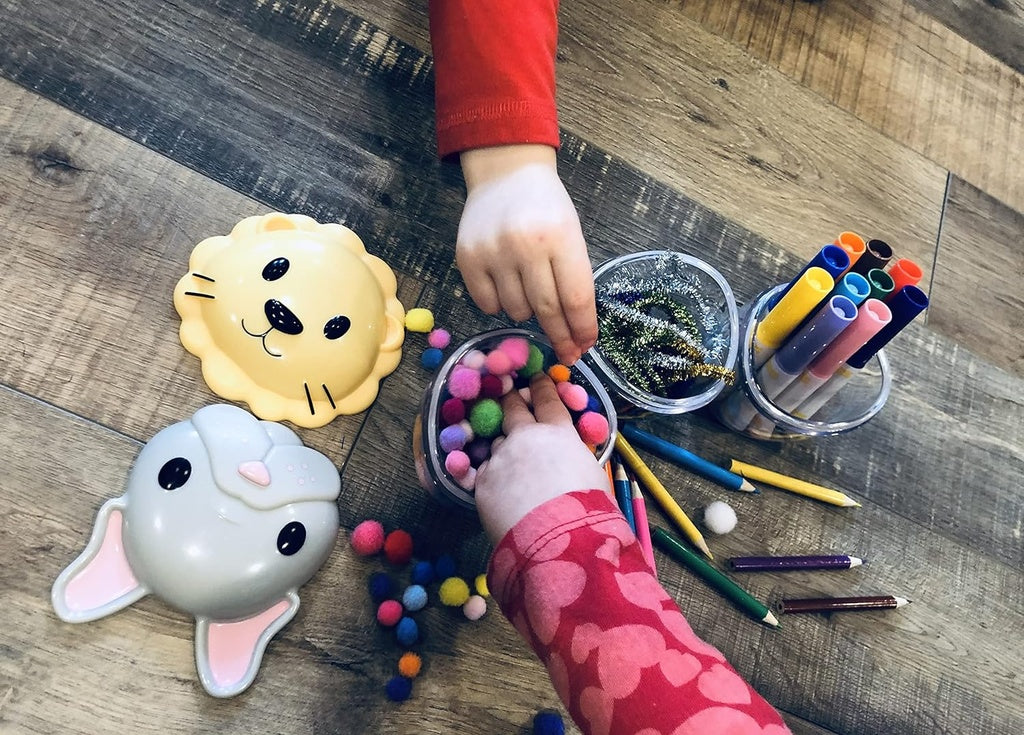 Children's hands playing with colorful pom-poms and art supplies on a wooden surface.