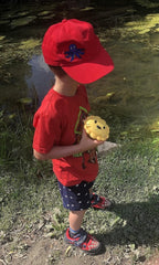 Child in a red shirt and cap holding a yellow Meliii snack container.