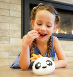Young girl eating near a panda-shaped Meli Snack Container.