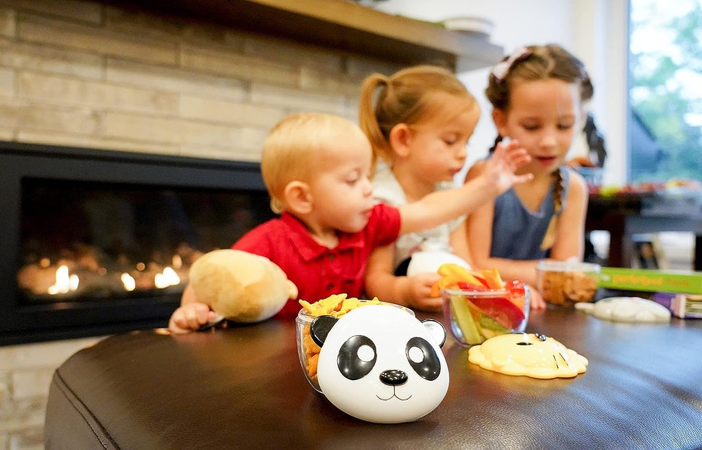 Children sitting at a table with food and a panda-themed container in a cozy indoor setting.