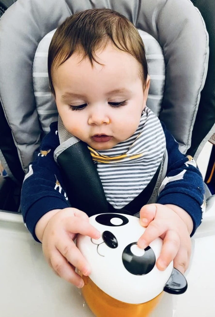 Baby sitting in a high chair holding a Melii snack container with a focus on the toy's design.