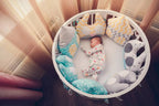 Baby sleeping in a round baby crib with colorful pillows and soft toys.