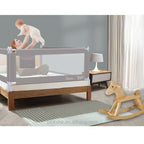 Baby being lifted by a parent over a bed with a safety rail.!