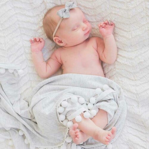 Newborn baby sleeping on a soft blanket with a gray headband.