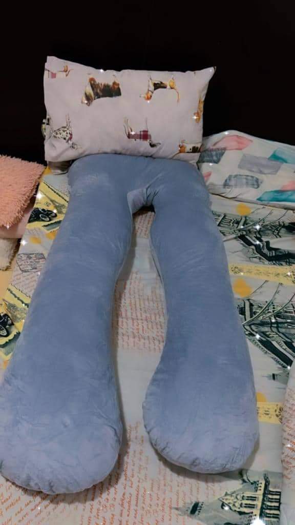 Gray U-shaped body pillow on a bed with a patterned pillow above it.