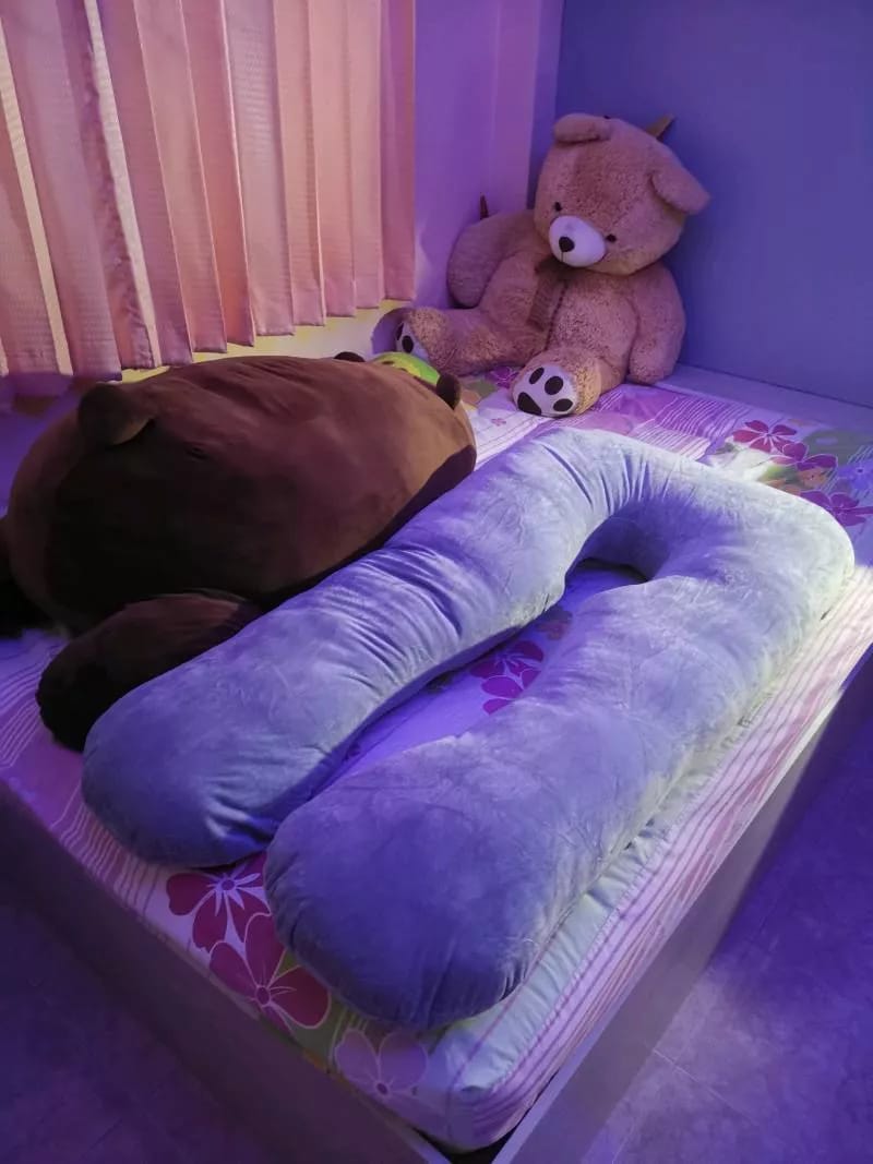 Purple U-shaped body pillow on a bed with teddy bears.