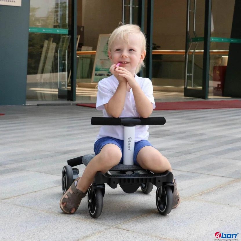 A young child sitting on a black and white  convertible rider l LT ride-on toy in front of a modern building entrance.